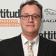 Russell T. Davies, in a black jacket and floral tie, stands before a placard reading attitude Magazine Foundation.